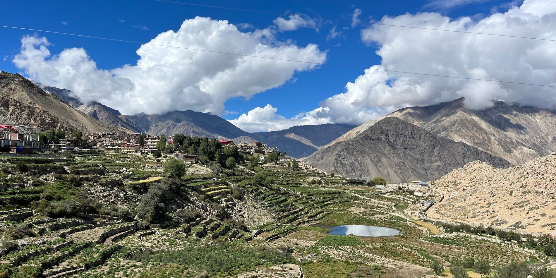 Farmland in a valley with mountains surrounding it and a cloudy blue sky overhead