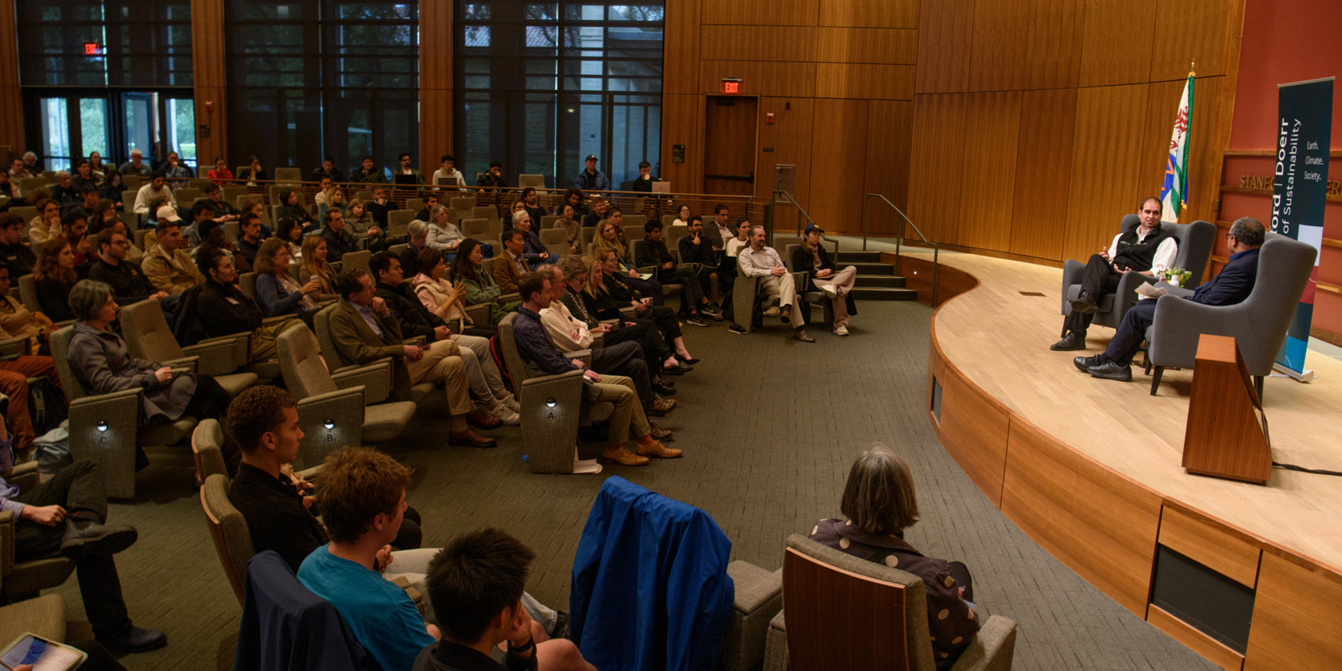 JB Straubel and Dean Arun Majumdar speak on stage in front of a large audience