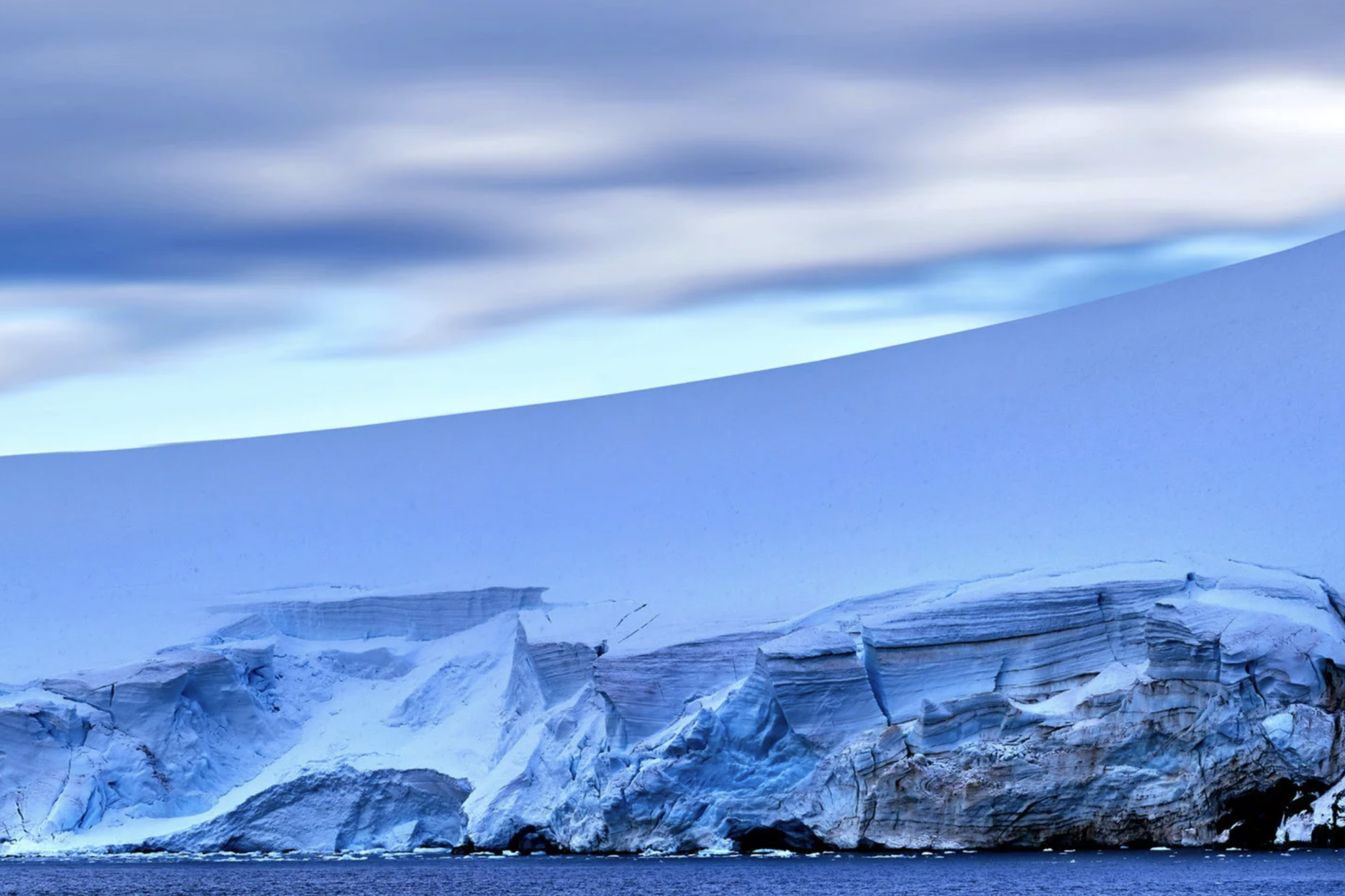 A glacier rises from calm seawater against a cloudy sky