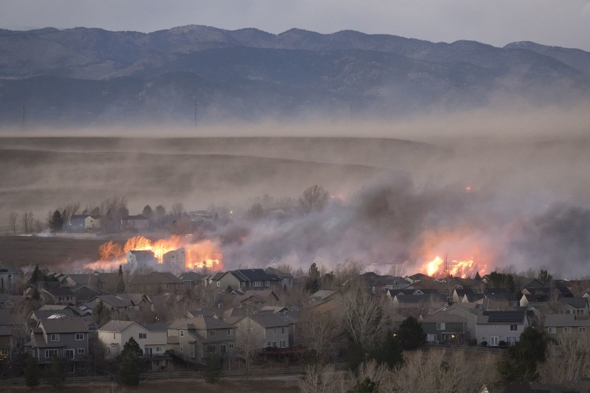 Homes and grasslands in flames with mountains in background
