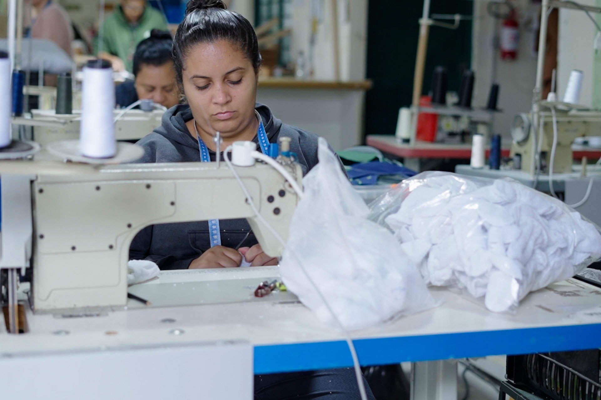 A woman works at a sewing machine with white fabric scraps.