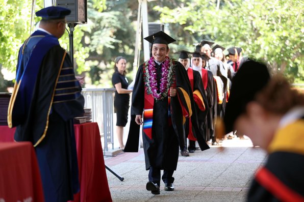 A student in a cap and gown smiles walking toward Arun Majumdar to receive their diploma