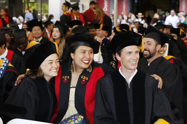 A group of three students smiling for a photo while sitting in their seats at commencement