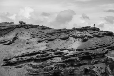 Two travelers pause above one of the famous green sand beaches on the south side of the big island of Hawai’i, their jeep parked precariously on the edge of the cliff.