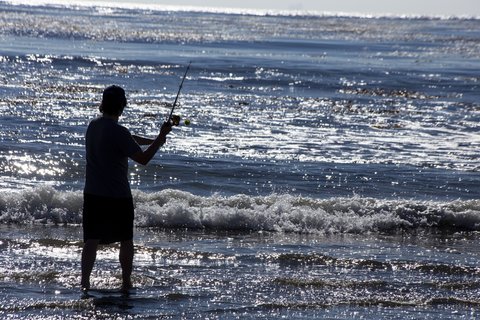 A person casts a fishing rod into the surf.