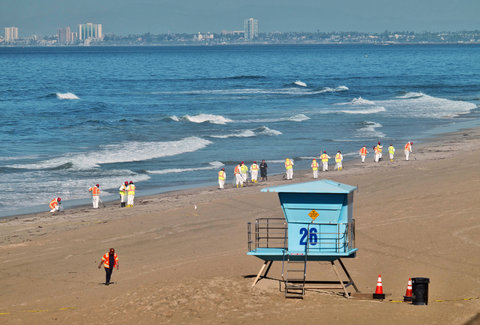 Emergency personnel walk along the shoreline in Huntington Beach with a city skyline in the background