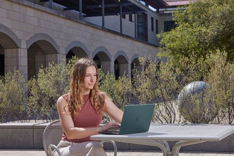Emily working on her laptop outside on campus