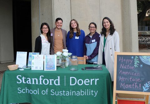 The DEI team smiling behind a Stanford Doerr School of Sustainability table and Happy Native American Heritage Month sign