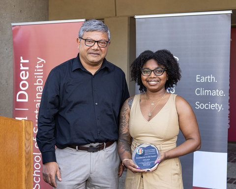 Alexis Wilson smiling on stage holding the Excellence in DEI award with Arun Majumdar