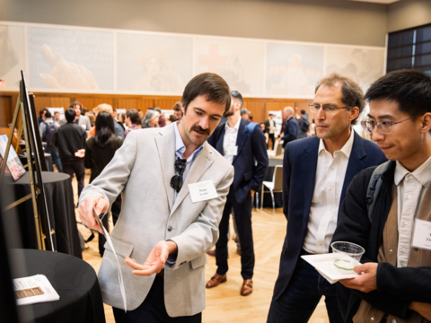 A researcher gestures and describes their work while two attendees listen during a poster session