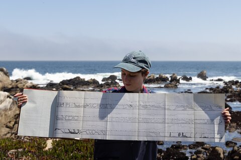 A researcher extends her arms wide to hold up the 1934 graduate thesis of Willis Hewatt.