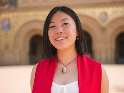 Chloe Cheng smiling outside Memorial Church in a red graduation stole