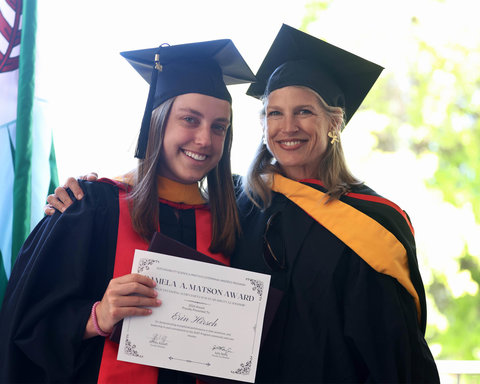 A graduating student holding their award and smiling with a faculty member