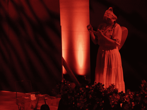 Dramatic red lighting on a stage as an actor wearing a mask in a field of strawberries looks up to the sky