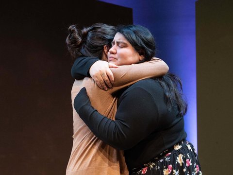 Two actors hugging tightly with sad expressions