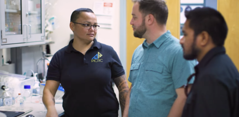 Three researchers stand in a lab with equipment in the background.