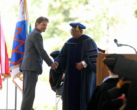 Kyle Douglas smiling and shaking hands with Dean Majumdar at the front of the commencement ceremony