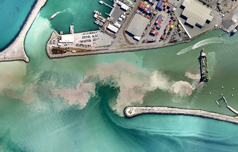 Aerial view of a dredging vessel near a shipping harbor leaving behind a large cloud of sediment