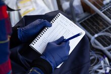 Gloved hand records observations in a spiral notebook