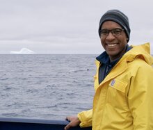 Earle Wilson in yellow jacket with ocean and iceberg in distance