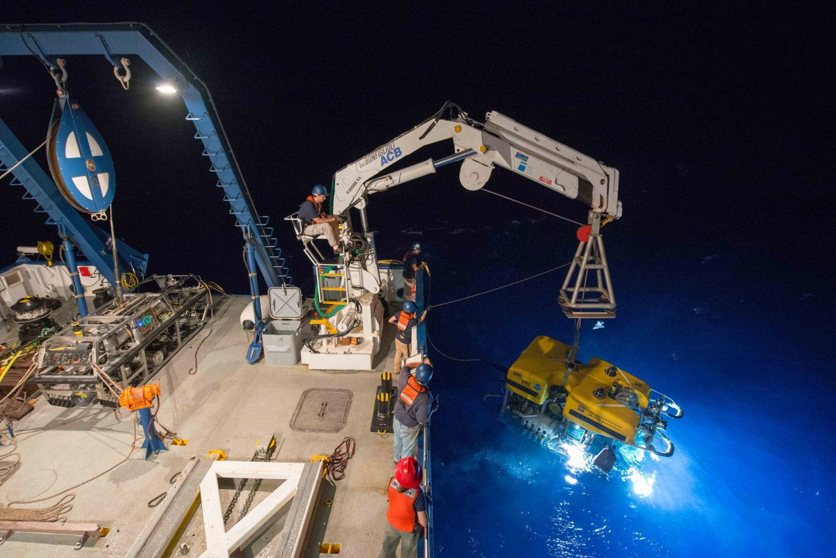 Crane lowering drone off of a ship at night