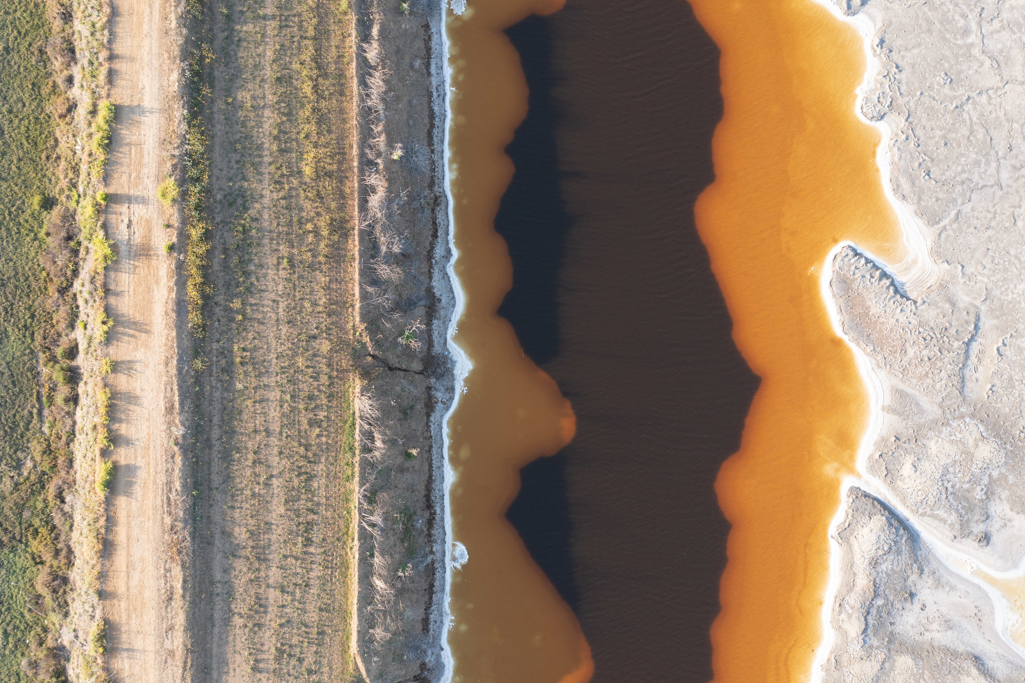 Birds eye view. Vertical lines of a grassy dirt path parallel to wavy yellow and black trails in water