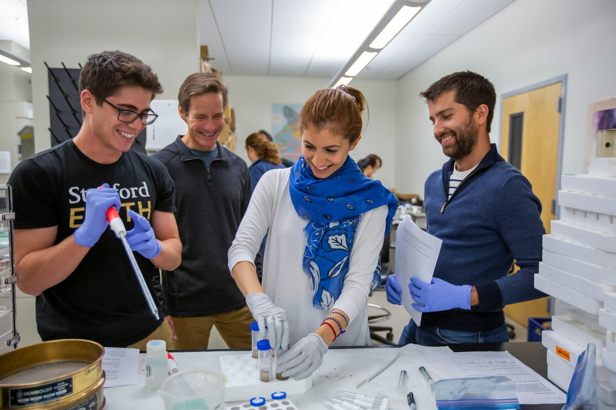 Three students work in a lab with a professor overseeing