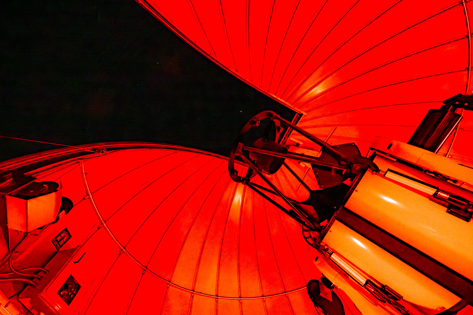 View looking up at the open roof of an observatory. Red-orange panels and curved lines of the roof frame the night sky