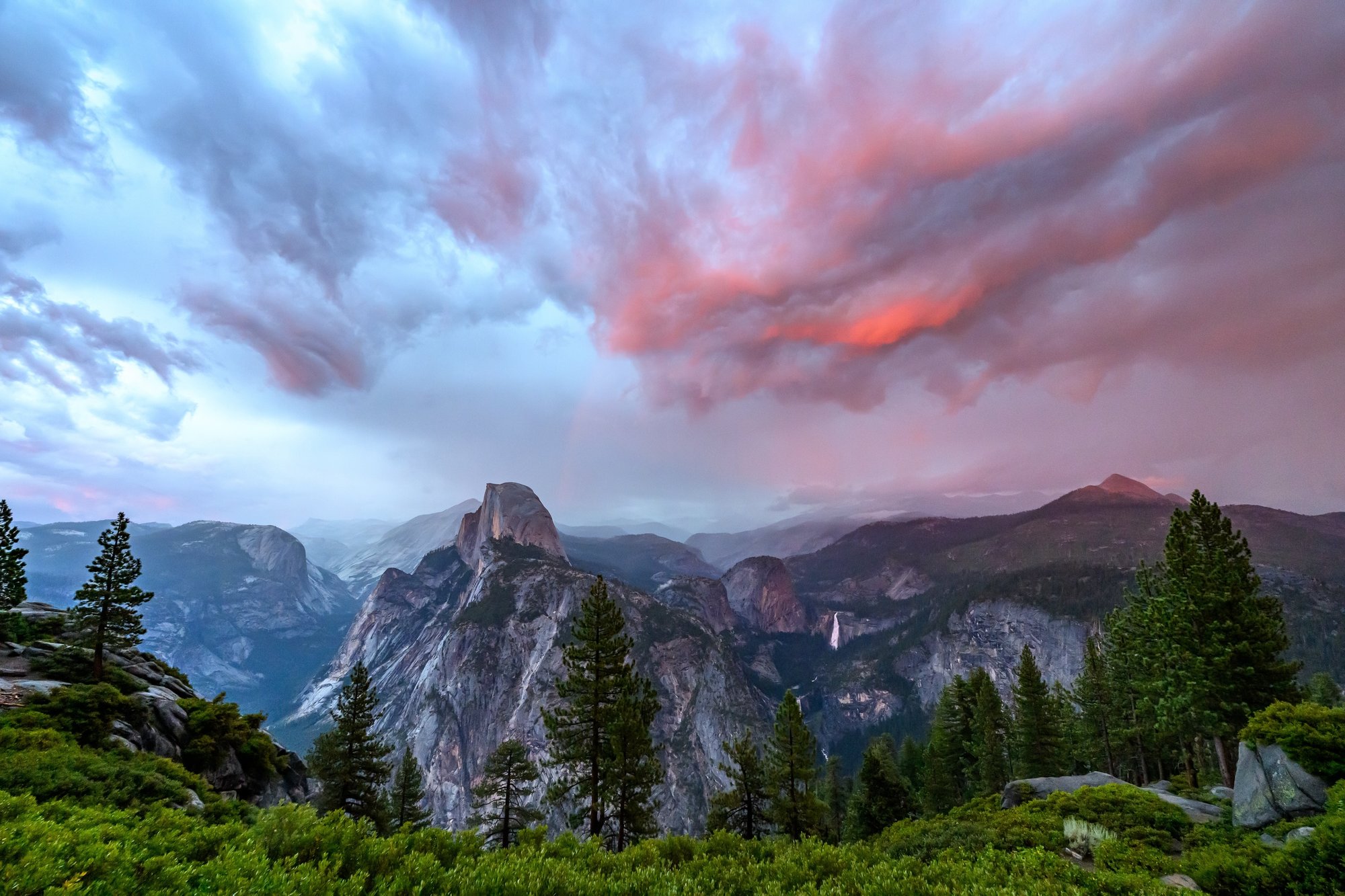 Dark clouds outlined by the sunset's glow sweep over a mountain landscape